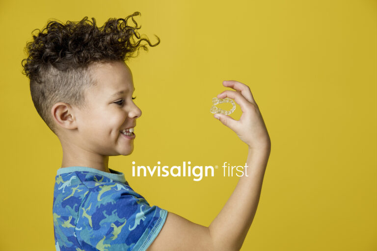 Young boy holding Invisalign clear aligner on yellow background with Invisalign First logo in white