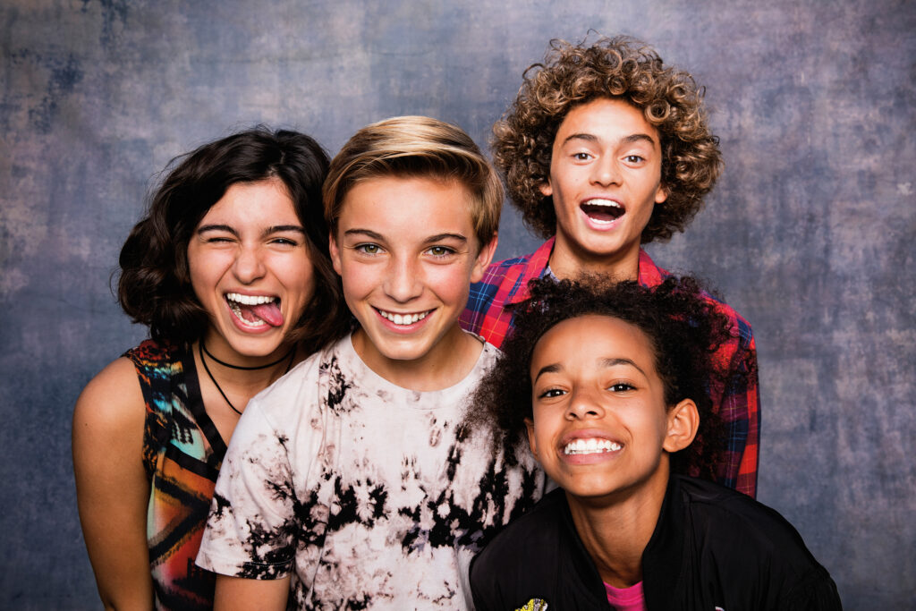 Four teenagers smiling and goofing off at the camera with a blue photobooth background