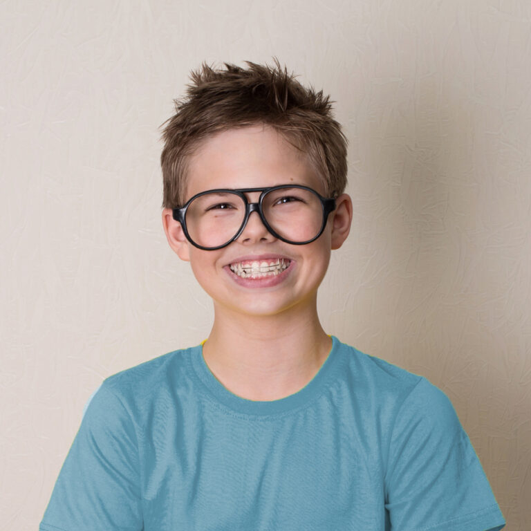 Young boy wearing blue t-shirt and black glasses smiling wearing orthodontic appliance