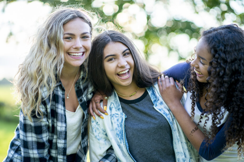 Three teenage girls of different ethnicity outdoors embracing and smiling