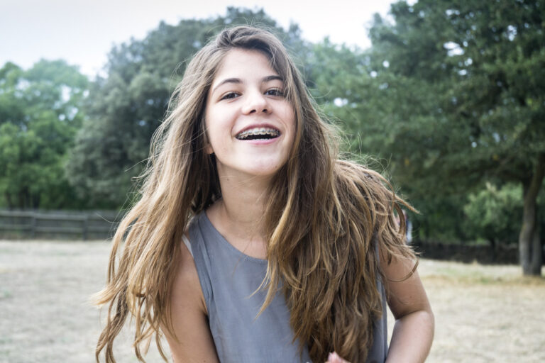 Teenage girl wearing gray tank top smiling with braces in nature